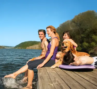 A happy family of two adults and two children sits on a dock by a lake, enjoying an allergy free sunny day.
